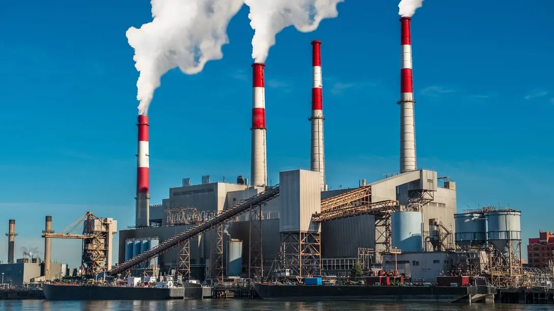A coal-fired generating station on the waterfront, four stacks venting and a coal conveyor running up to the boiler house