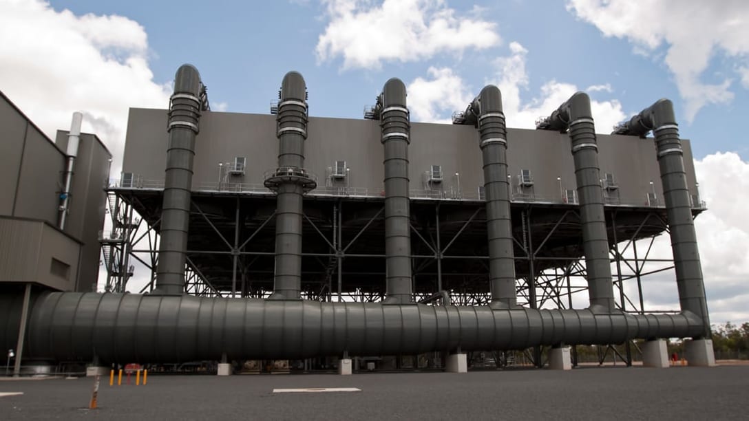 An air-cooled condenser bank raised on a steel structure, fed by six exhaust duct risers off a ground-level main